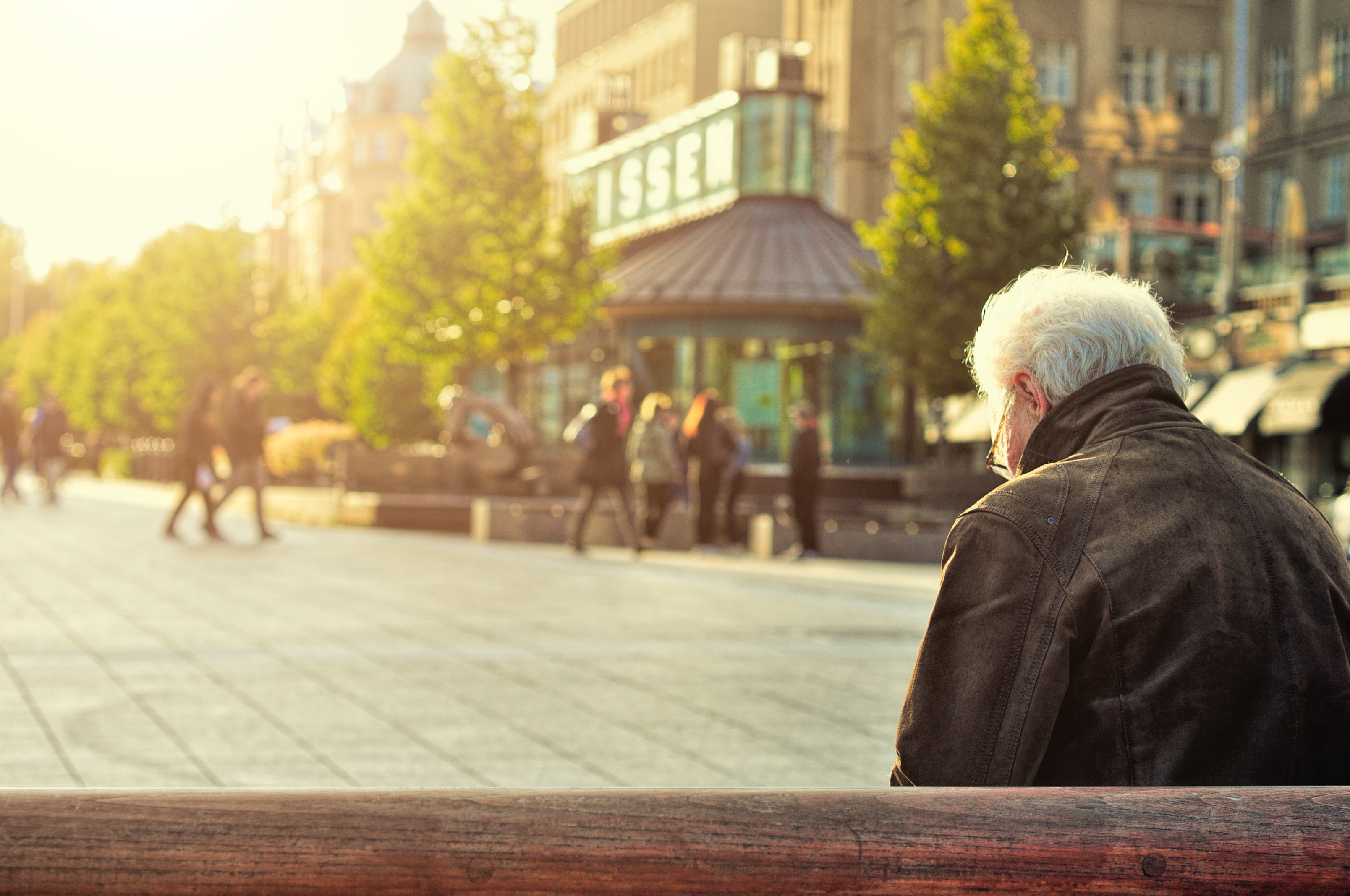 A man sits alone on a bench in a crowded high street