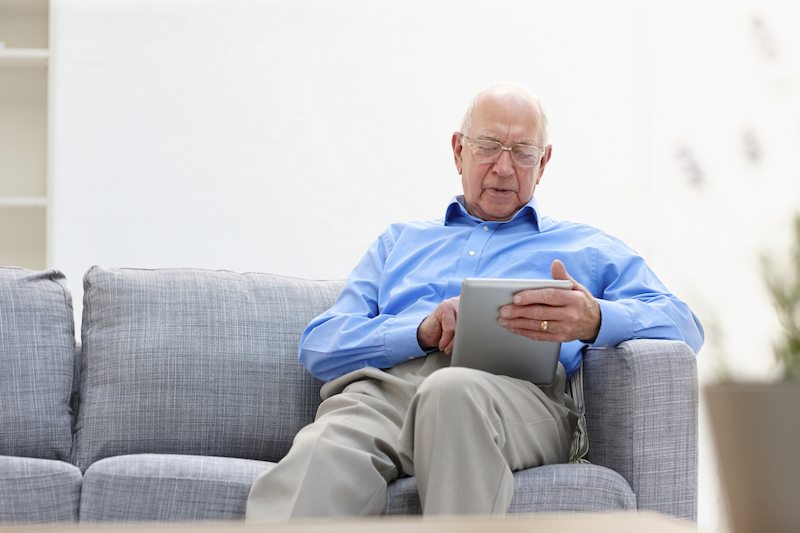 older man usinga. tablet on his sofa