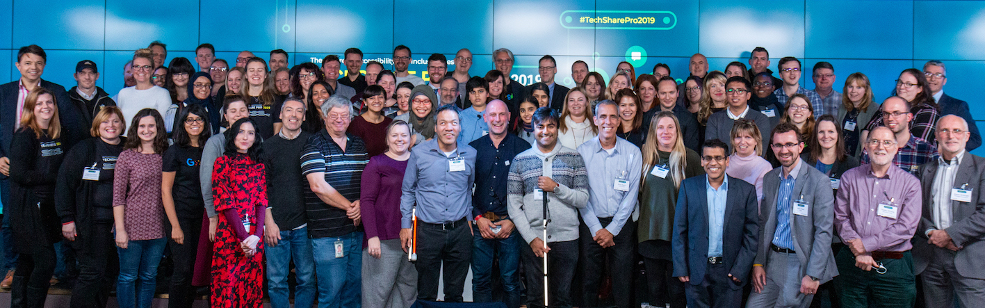 Group shot of attendees at the end of TechShare Pro 2019, standing together on stage smiling at the camera