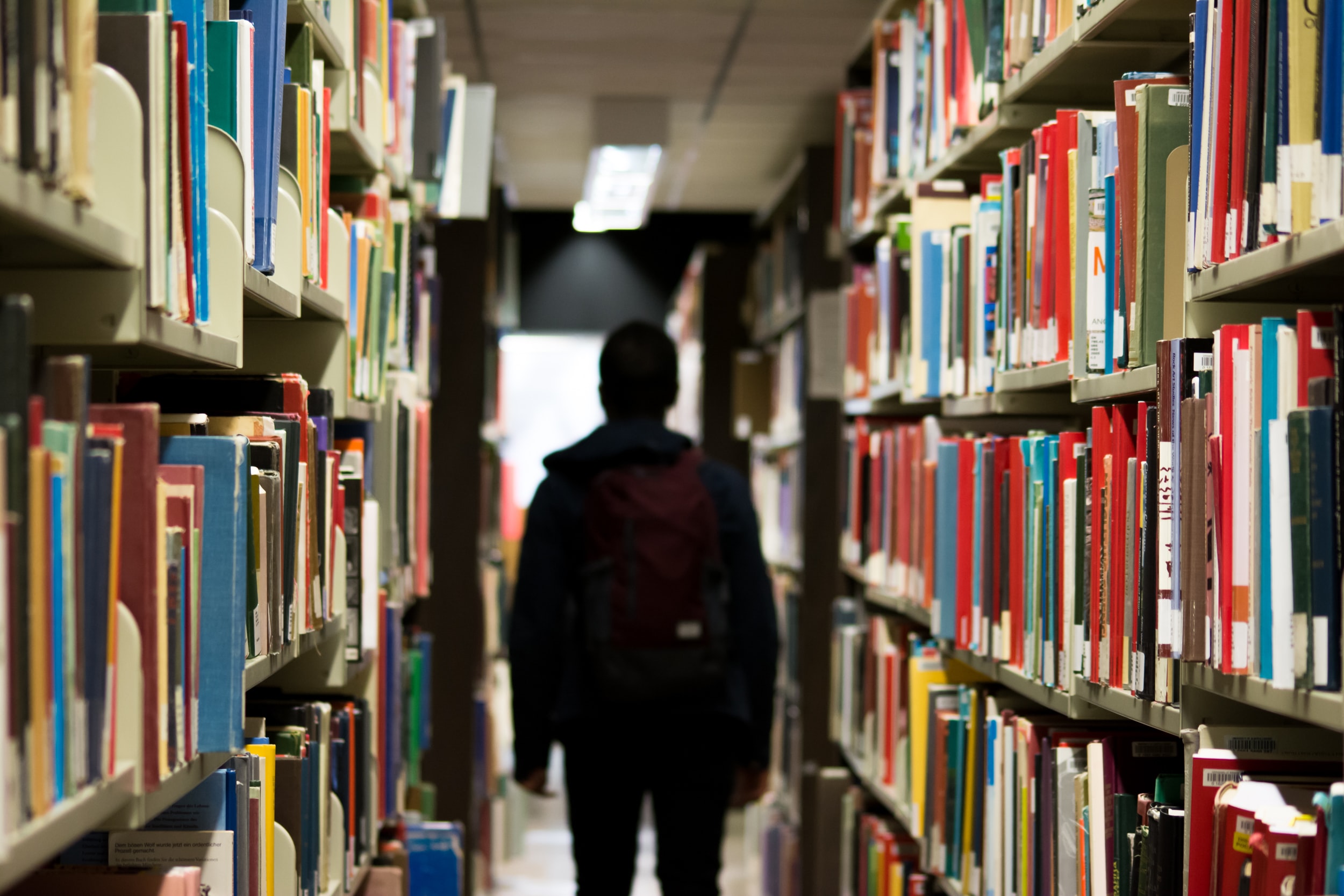 Student standing in library between shelves of books