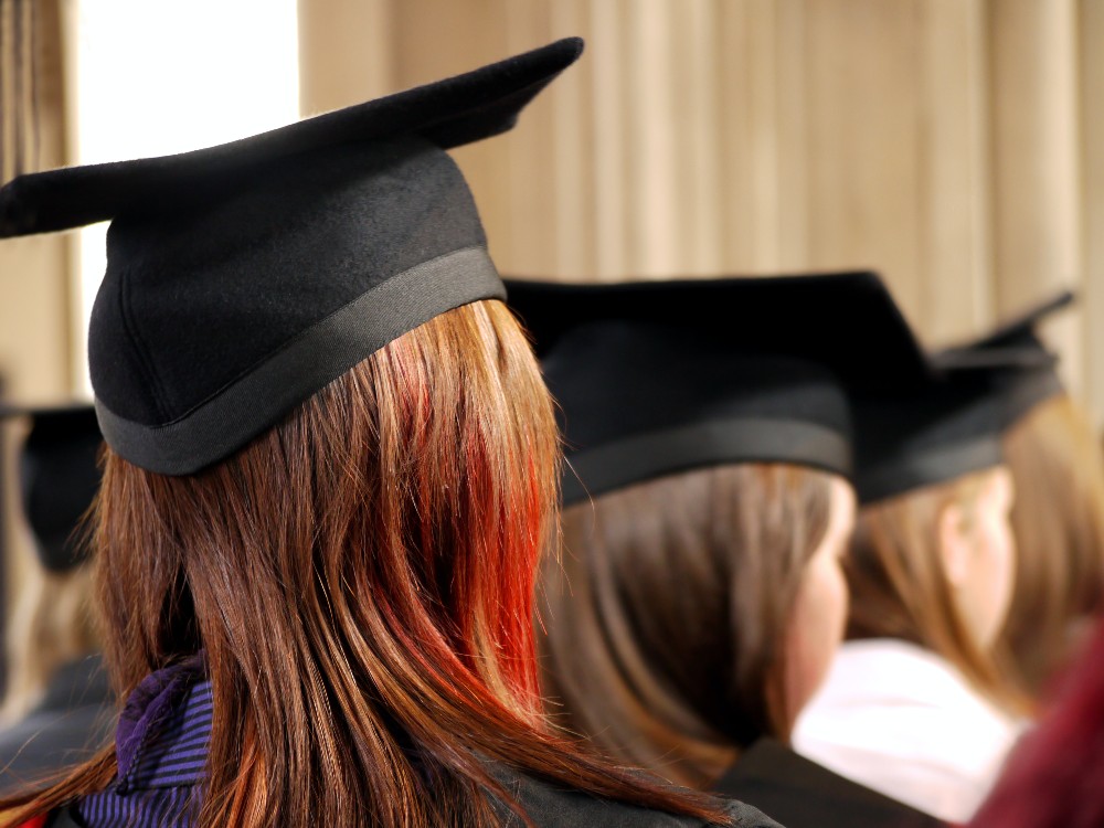 backs of heads of group of female students wearing graduation gowns and hats 