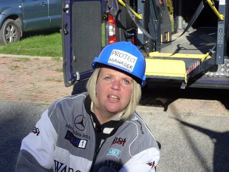 A photo of laura in front of a vehicle wearing safety gear with the label 'Project Manager' on her hard hat