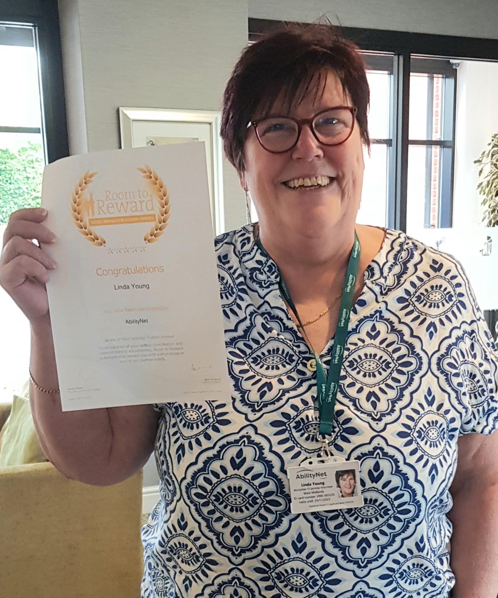 Linda Young smiling, holding her Room to Reward certificate