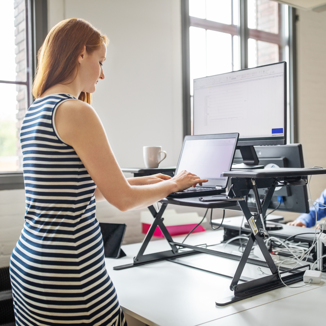 A person standing at their sit-stand desk in an office.