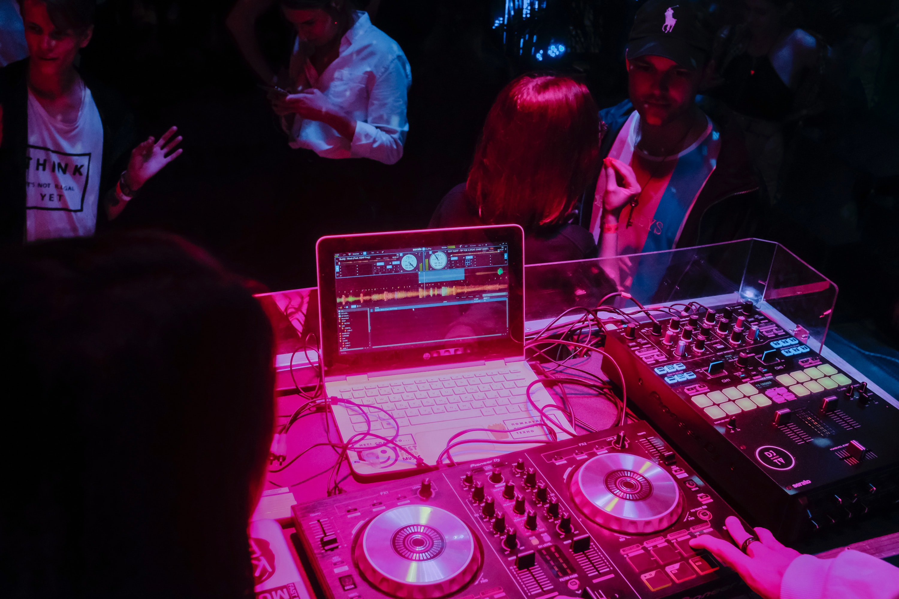 Image shows a laptop attached to DJ decks, people are dancing in the background