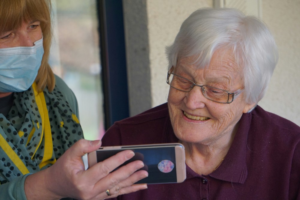 Woman in mask showing an elderly woman something on a smartphone, smiling