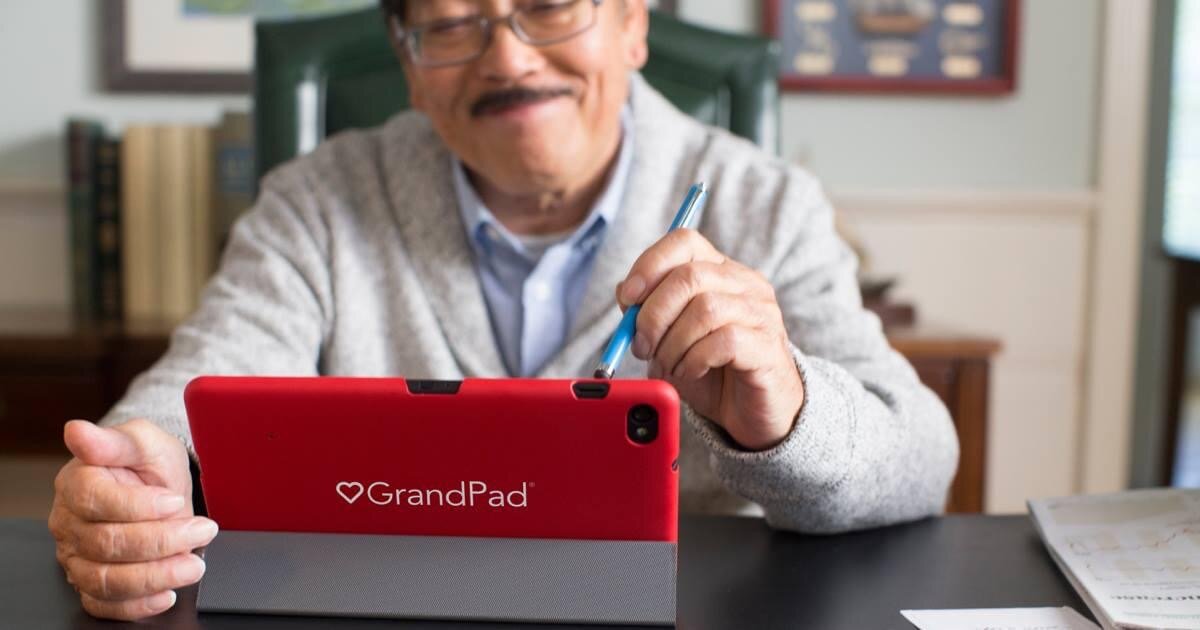 A picture of an older gentleman using the GrandPad on a table. He holds a stylus.