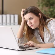 young woman sat at laptop looking frustrated