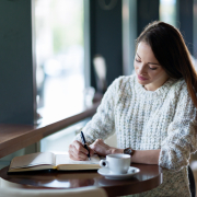 student looking relaxed writing in cafe with hot drink