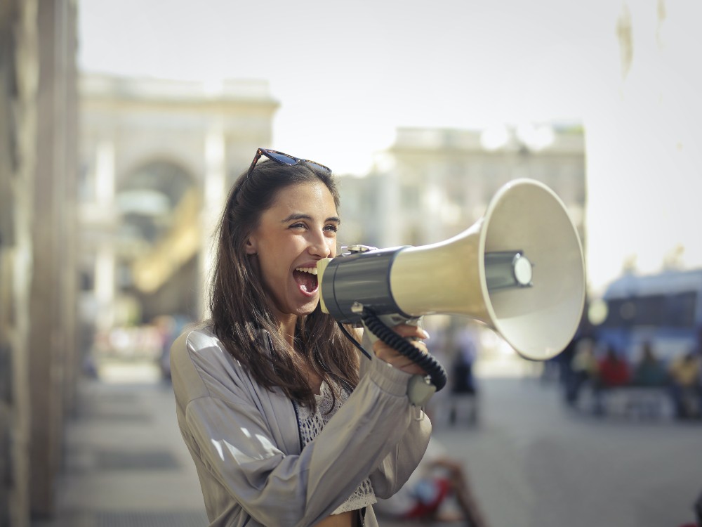 Woman in street holding loudspeaker to her mouth and talking into it