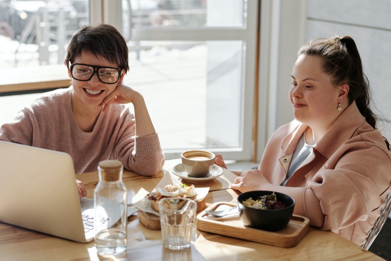 Two women looking at computer and smiling over breakfast table