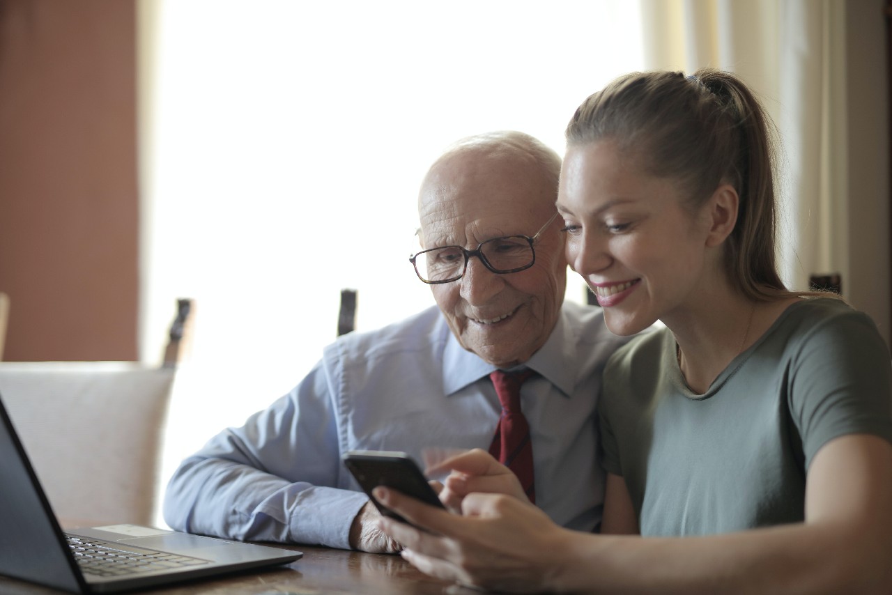 Older man looking at device and smiling with younger woman also looking at phone